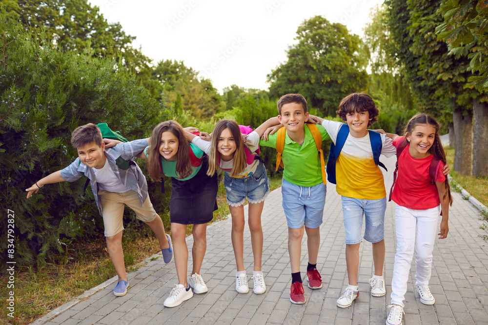 Group of friends having fun together. Six happy children playing outside after school. Several elementary students in casual clothes standing on park path, hugging, smiling and looking at camera Group of friends having fun together. Six happy children playing outside after school. Several elementary students in casual clothes standing on park path, hugging, smiling and looking at camera