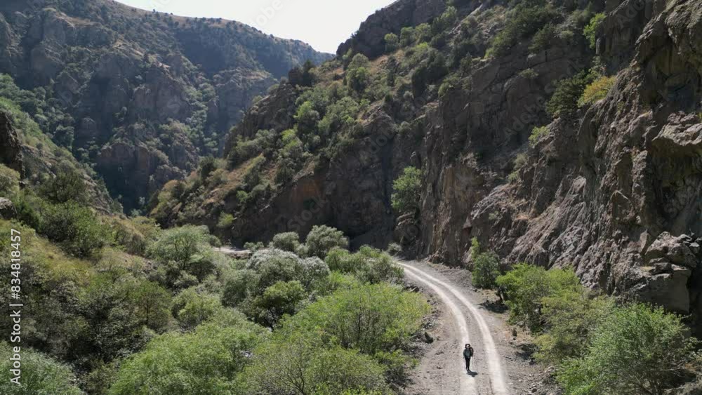 Backpacker hikes on dirt road in rugged narrow rock canyon, high angle Backpacker hikes on dirt road in rugged narrow rock canyon, high angle