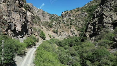 Aerial follows backpacker hiking on gravel road in rustic rock canyon photo