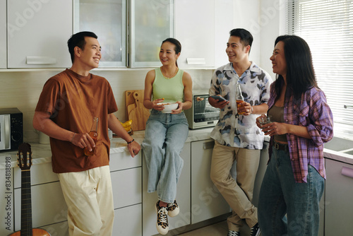 Valokuva Friends casually talking and snacking in a bright, modern kitchen, creating a wa