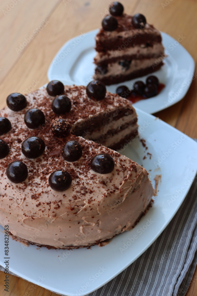 Sliced chocolate cake with cocoa cream and sour cherries in syrup decoration on a white plate on woodne table Sliced chocolate cake with cocoa cream and sour cherries in syrup decoration on a white plate on woodne table