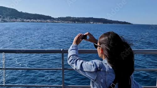 Young brunette woman with hair flying in the wind and glasses films the blue sea