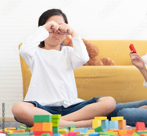 Adorable Asian kid playing wooden blocks with her sister on the floor of living room. Happy sibling children have fun playing game toy together at home. with colorful blocks. Playful girls enjoyment.