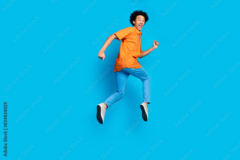 Full length photo of attractive funny guy wear orange shirt running jumping high emtpy space isolated blue color background Full length photo of attractive funny guy wear orange shirt running jumping high emtpy space isolated blue color background