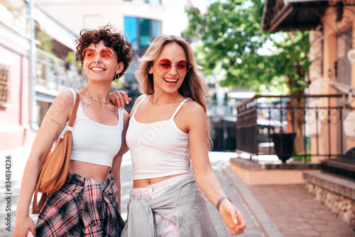 Two young beautiful smiling hipster female in trendy summer white t-shirt and shorts clothes. Sexy carefree women posing in the street. Positive models having fun, hugging and going crazy