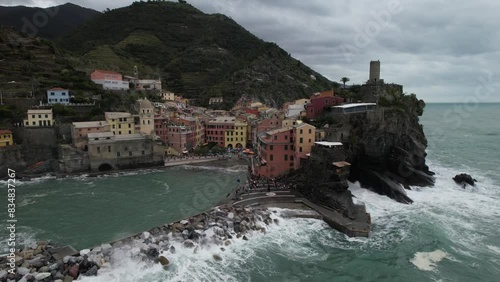 ORBITAL DRONE SHOT LEFT TO RIGHT OF CINQUE TERRE ITALIAN VILLAGE BY THE BEACH WAVES CRASHING LOW ANGLE photo