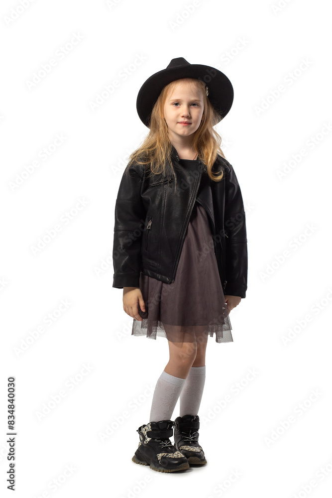 A little blonde girl in a leather jacket and a black hat poses in the studio isolated on a white background. A little blonde girl in a leather jacket and a black hat poses in the studio isolated on a white background.