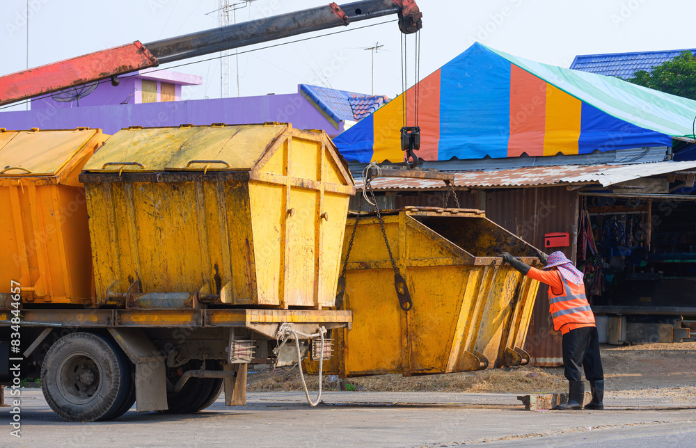 Asian garbage worker is moving yellow metal dumpster on garbage truck into public dumping area at suburb community Asian garbage worker is moving yellow metal dumpster on garbage truck into public dumping area at suburb community