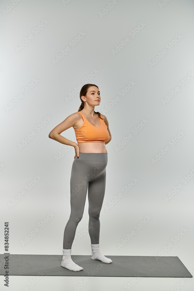 Fototapeta premium A sporty pregnant woman in workout attire stands confidently on a mat with hands on hips, showcasing her strength and vitality.