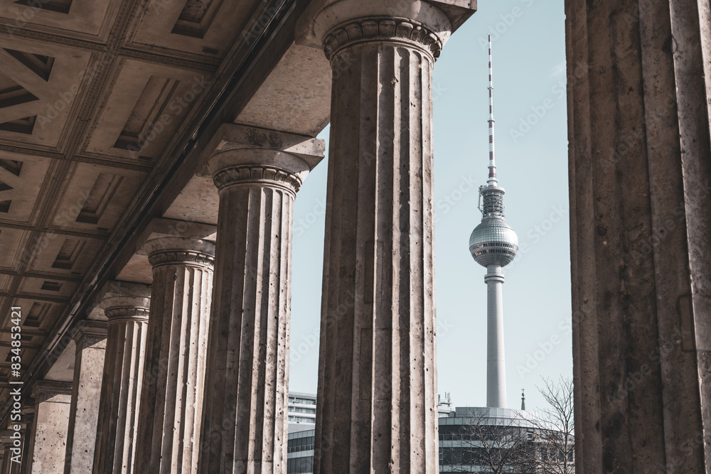 Φωτογραφία The Berlin TV Tower stands tall, framed by the classical columns of a nearby historical building on a clear day
