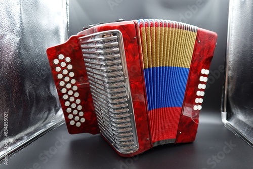 A vibrant red Colombian vallenato accordion featuring the colors of the Colombian flag (red, yellow, and blue). This traditional musical instrument is commonly used in Colombian folk music and is char