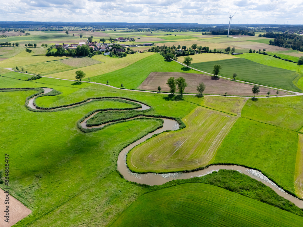 Drone shot of a wide european valley in which a small stream winds its way through green meadows and fields. Drone shot of a wide european valley in which a small stream winds its way through green meadows and fields.