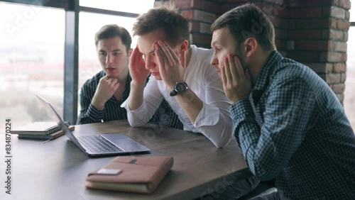 A group of three young men in the office, puzzled and bewildered by the work they're d, laptops.
