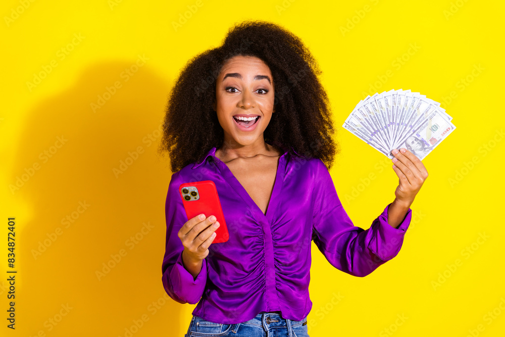 Photo portrait of lovely young lady hold telephone money fan dressed stylish violet garment isolated on yellow color background Photo portrait of lovely young lady hold telephone money fan dressed stylish violet garment isolated on yellow color background