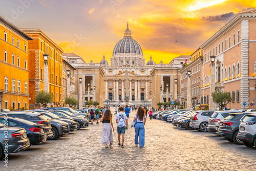 A group of tourists walk towards the Vatican City along the Road of Conciliation during a golden sunset.