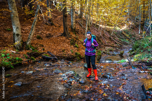Tourist woman with backpack in rubber boots hiking on the forest stream