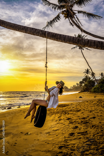 Woman having fun on tire swing on tropical beach at sunset