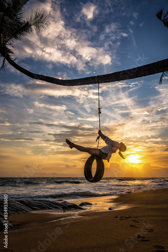 Young tourist woman having fun on tire swing on tropical beach