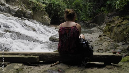 A female traveler enjoying the peaceful surroundings of Goa Rang Reng waterfall in Bali, Indonesia. Static slow motion shot. photo