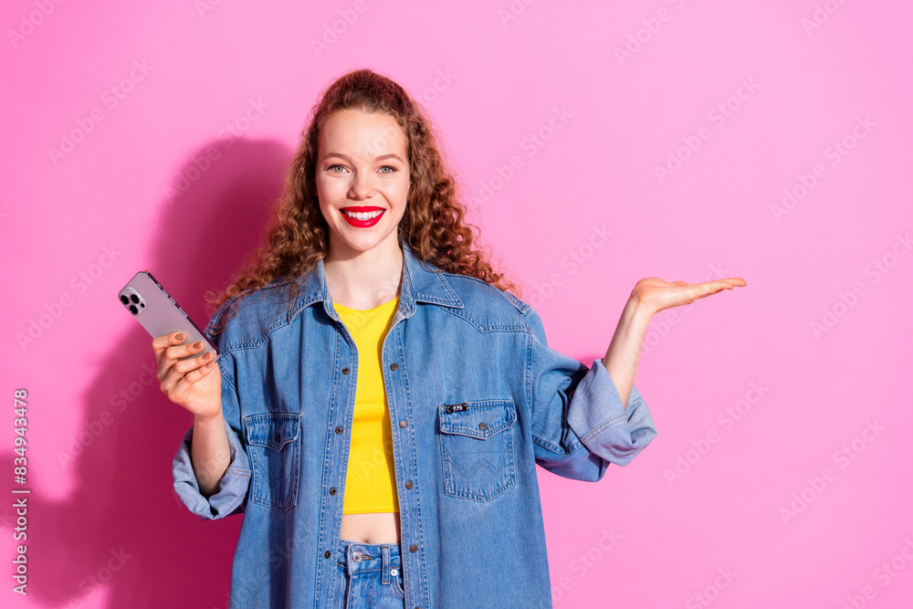 Photo of charming positive girl wear jeans shirt texting modern device holding arm empty space isolated pink color background Photo of charming positive girl wear jeans shirt texting modern device holding arm empty space isolated pink color background