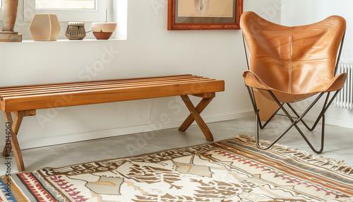 A living room with a teak wood slat bench, a leather butterfly chair in tan, and a geometric patterned kilim rug photo