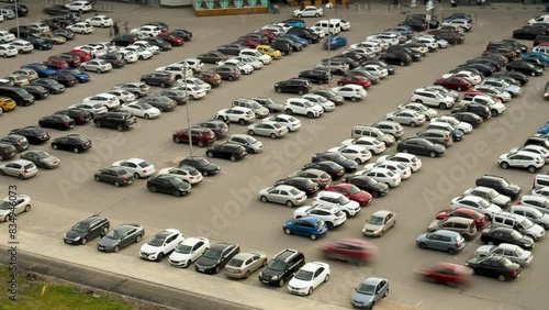 Time-lapse cars quickly park and drive away during the day in a parking lot next to a shopping center, top view, long shot photo