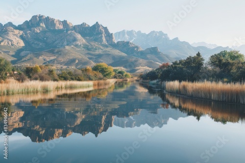 A tranquil scene of a glassy river reflecting the majestic  towering mountains in the distance.