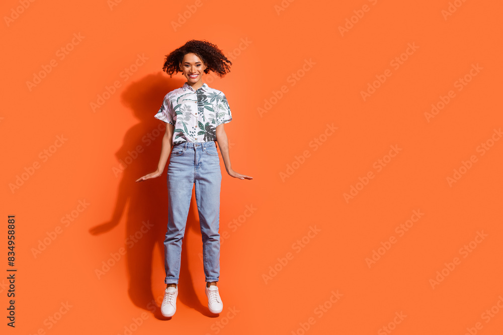 Full body length photo of american woman in jeans and summer stylish shirt jumping air with good vibes isolated on orange color background Full body length photo of american woman in jeans and summer stylish shirt jumping air with good vibes isolated on orange color background