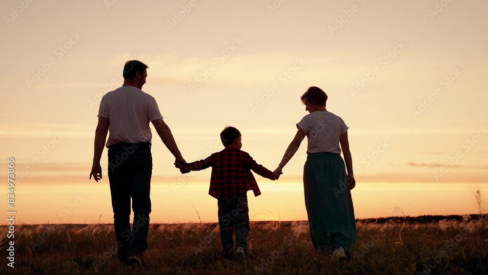 Parents hold their child hands in park. Happy family mom dad child walking on summer evening. Small kid holds his parents hands. Concept family holidays. Dad son mom walking in meadow, sunset in sky