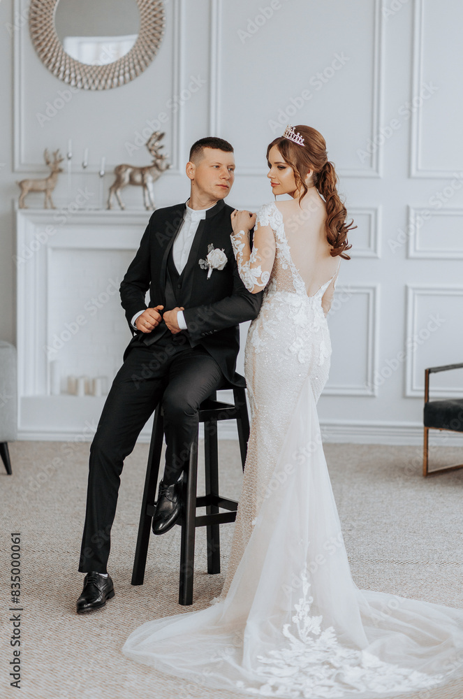 A man and a woman are posing for a picture in a room with a fireplace. The man is wearing a suit and tie, while the woman is wearing a wedding dress. Scene is romantic and celebratory A man and a woman are posing for a picture in a room with a fireplace. The man is wearing a suit and tie, while the woman is wearing a wedding dress. Scene is romantic and celebratory