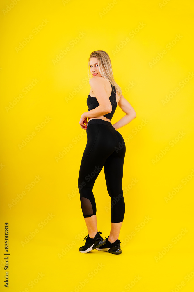 Fit sportswoman in leggings and sports bra looking away and while standing on yellow red Fit sportswoman in leggings and sports bra looking away and while standing on yellow red