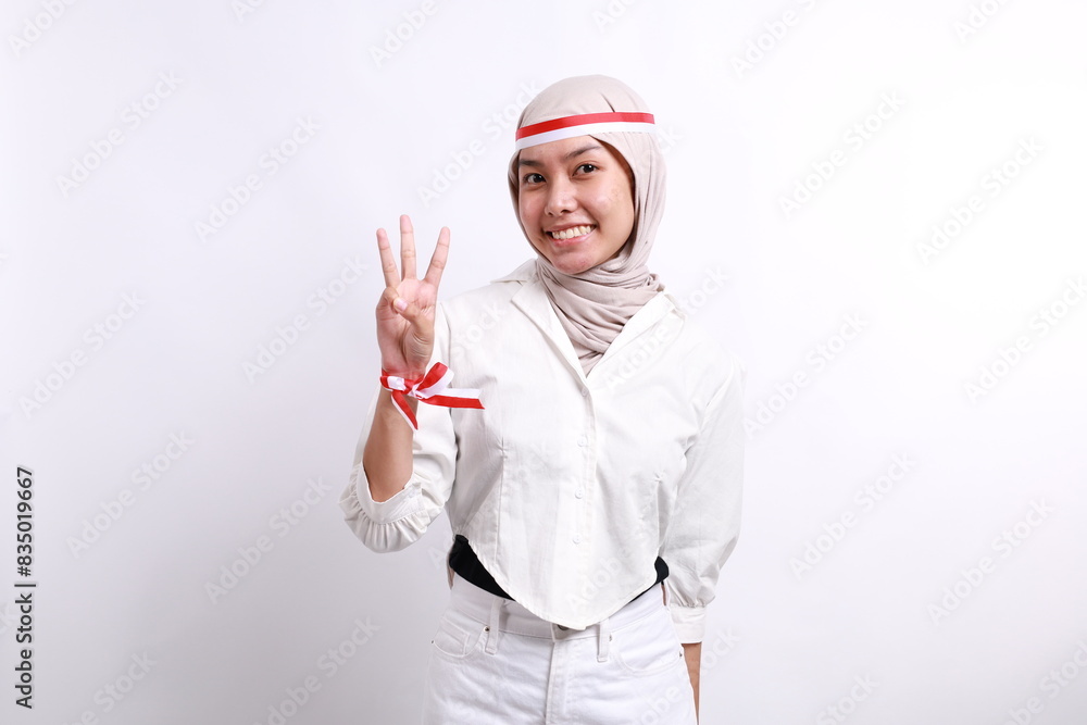 Asian young asian muslim woman with red white ribbon for celebrating Indonesia independence day standing while showing three fingers Asian young asian muslim woman with red white ribbon for celebrating Indonesia independence day standing while showing three fingers