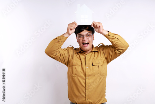 Portrait of Happy government worker or pegawai negeri sipil or pns wearing khaki uniform standing while holding home paper craft photo