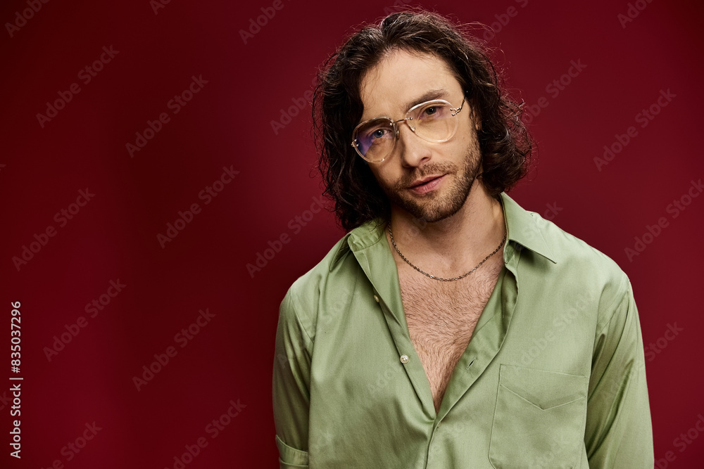 A handsome man wearing glasses and a green silk shirt poses against a vibrant red background. A handsome man wearing glasses and a green silk shirt poses against a vibrant red background.