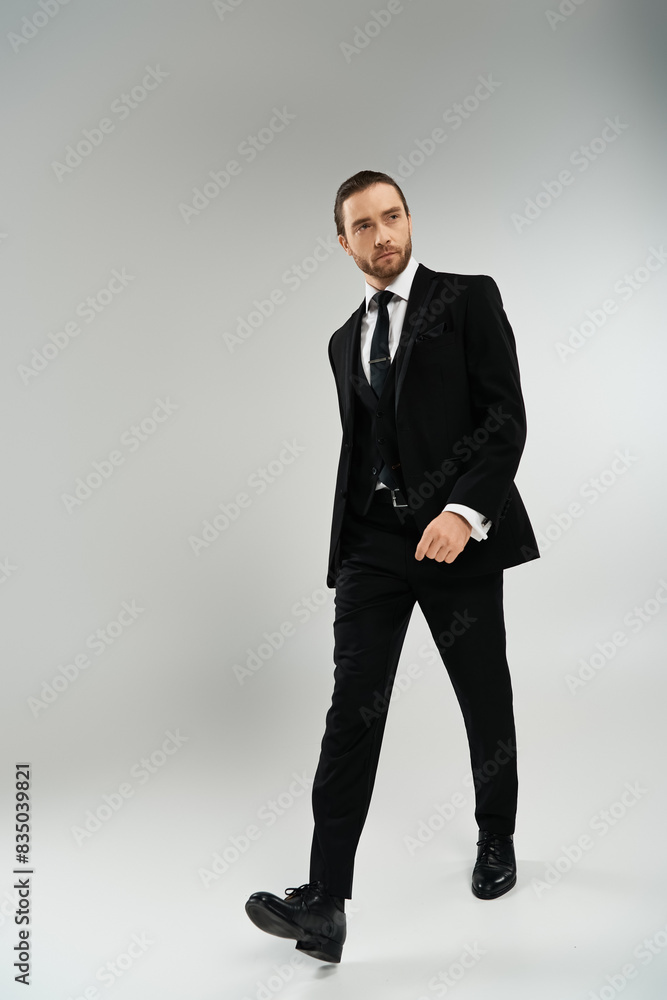 A bearded businessman confidently walks in a suit and tie against a grey studio backdrop. A bearded businessman confidently walks in a suit and tie against a grey studio backdrop.