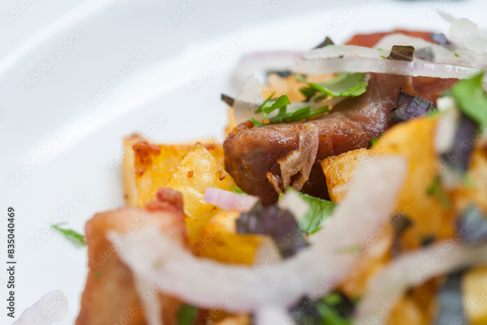 Fried meat with potatoes, onion and herbs on a white plate Fried meat with potatoes, onion and herbs on a white plate