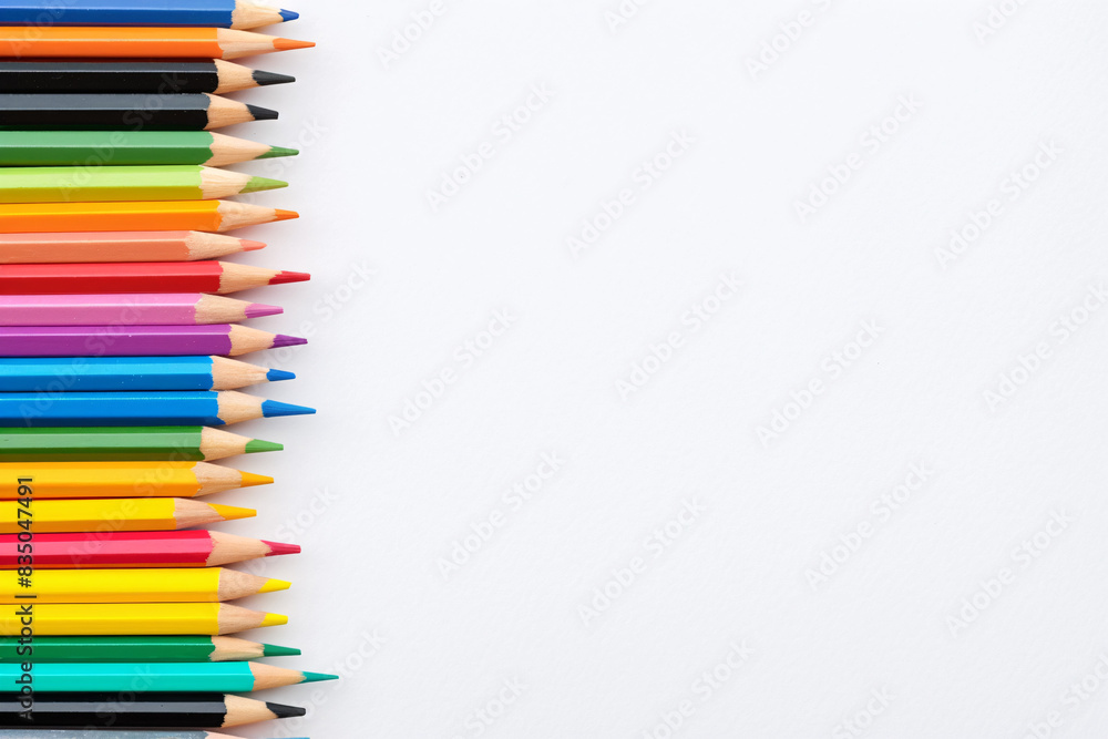 Colorful pencils arranged in a neat row on a plain white background with sharpened tips pointing to the right Colorful pencils arranged in a neat row on a plain white background with sharpened tips pointing to the right