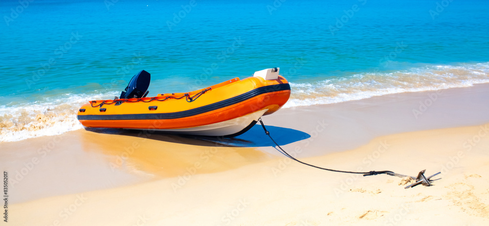 An inflatable motor boat is moored with an anchor on the sandy seashore. An inflatable motor boat is moored with an anchor on the sandy seashore.