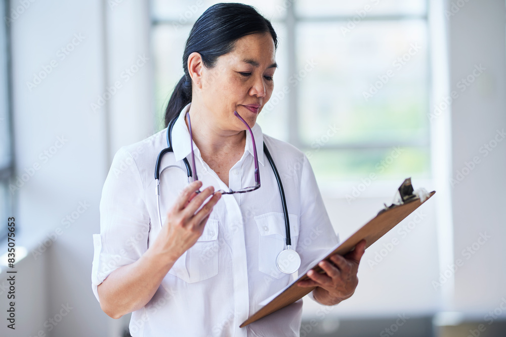 Asian Female Doctor Reviewing Patient Records in Hospital Setting Asian Female Doctor Reviewing Patient Records in Hospital Setting