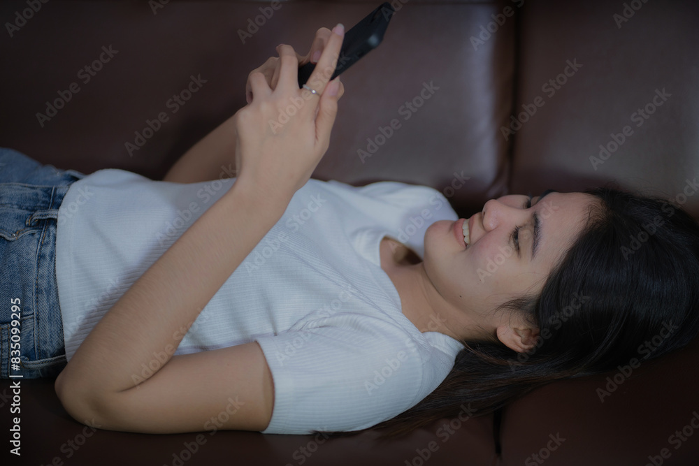 Happy young asian woman relaxing at home.Girl lying down looking at the phone, close-up. Woman use of smart phone and lying down on sofa Happy young asian woman relaxing at home.Girl lying down looking at the phone, close-up. Woman use of smart phone and lying down on sofa