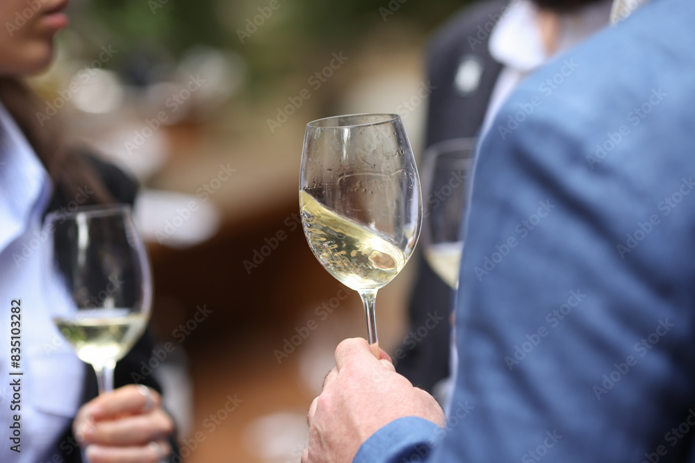 Shallow depth of field (selective focus) details with the hand of a man holding a glass of white wine at a party. Shallow depth of field (selective focus) details with the hand of a man holding a glass of white wine at a party.