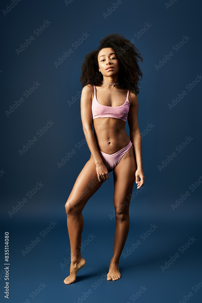 Young African American woman in a stylish pink bikini striking a pose against a vibrant blue backdrop.