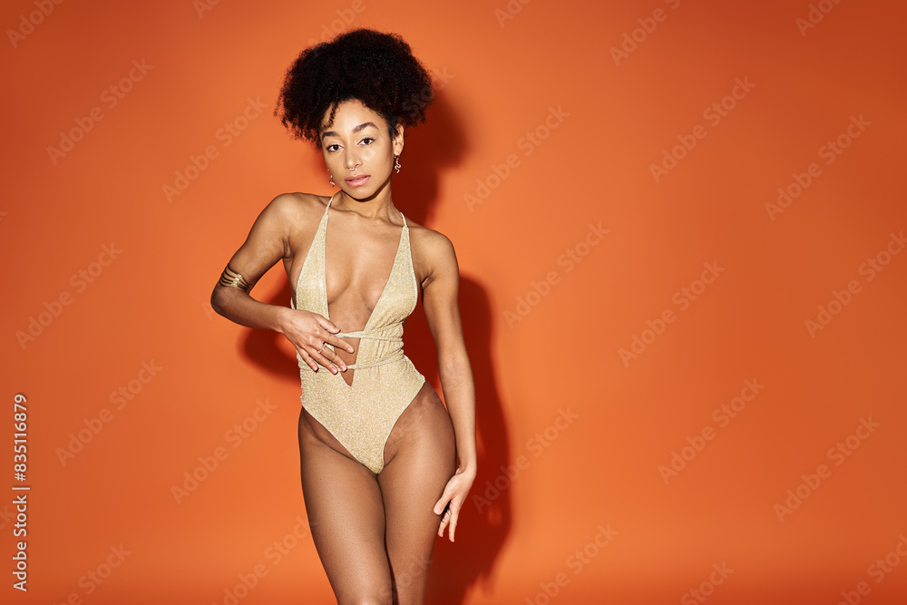 African American woman in trendy swimsuit poses against vivid orange backdrop. African American woman in trendy swimsuit poses against vivid orange backdrop.