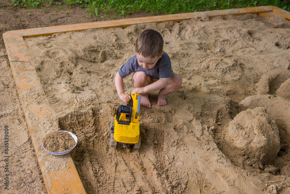 A little boy is playing with a toy dumper in the sand. A little boy is playing with a toy dumper in the sand.