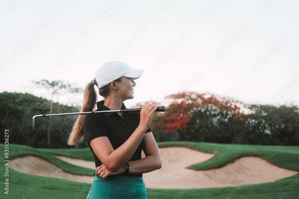Portrait of a young attractive woman who plays golf professionally on a green lawn. She is holding a golf club in her hands and looking at the side smiling. Luxurious summer sport. Portrait of a young attractive woman who plays golf professionally on a green lawn. She is holding a golf club in her hands and looking at the side smiling. Luxurious summer sport.