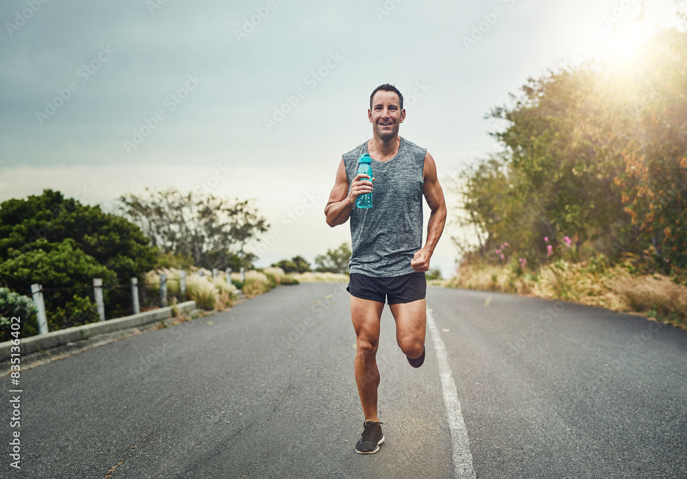Running, happy man and portrait with water bottle for exercise, cardio and fitness on road in nature. Male athlete, smile and workout on trail for health, sport or marathon training with sportswear Running, happy man and portrait with water bottle for exercise, cardio and fitness on road in nature. Male athlete, smile and workout on trail for health, sport or marathon training with sportswear