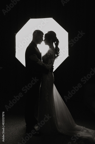A couple is kissing under a spotlight. The man is wearing a suit and the woman is wearing a wedding dress