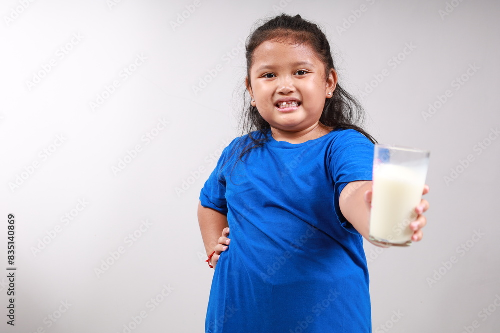 Adorable asian little girl standing while offering a glass of milk. Isolated on gray background with copyspace Adorable asian little girl standing while offering a glass of milk. Isolated on gray background with copyspace