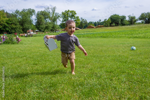 View from behind of little boy running barefoot on the grass in village