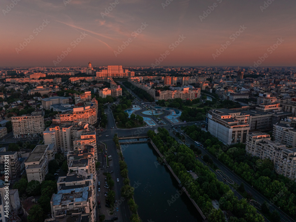 Naklejka premium Bucharest aerial photo. Beautiful view of the landmarks of Bucharest from Unirii area (boulevard, fountains and Palace of the Parliament) during a summer sunrise. Travel to Romania.